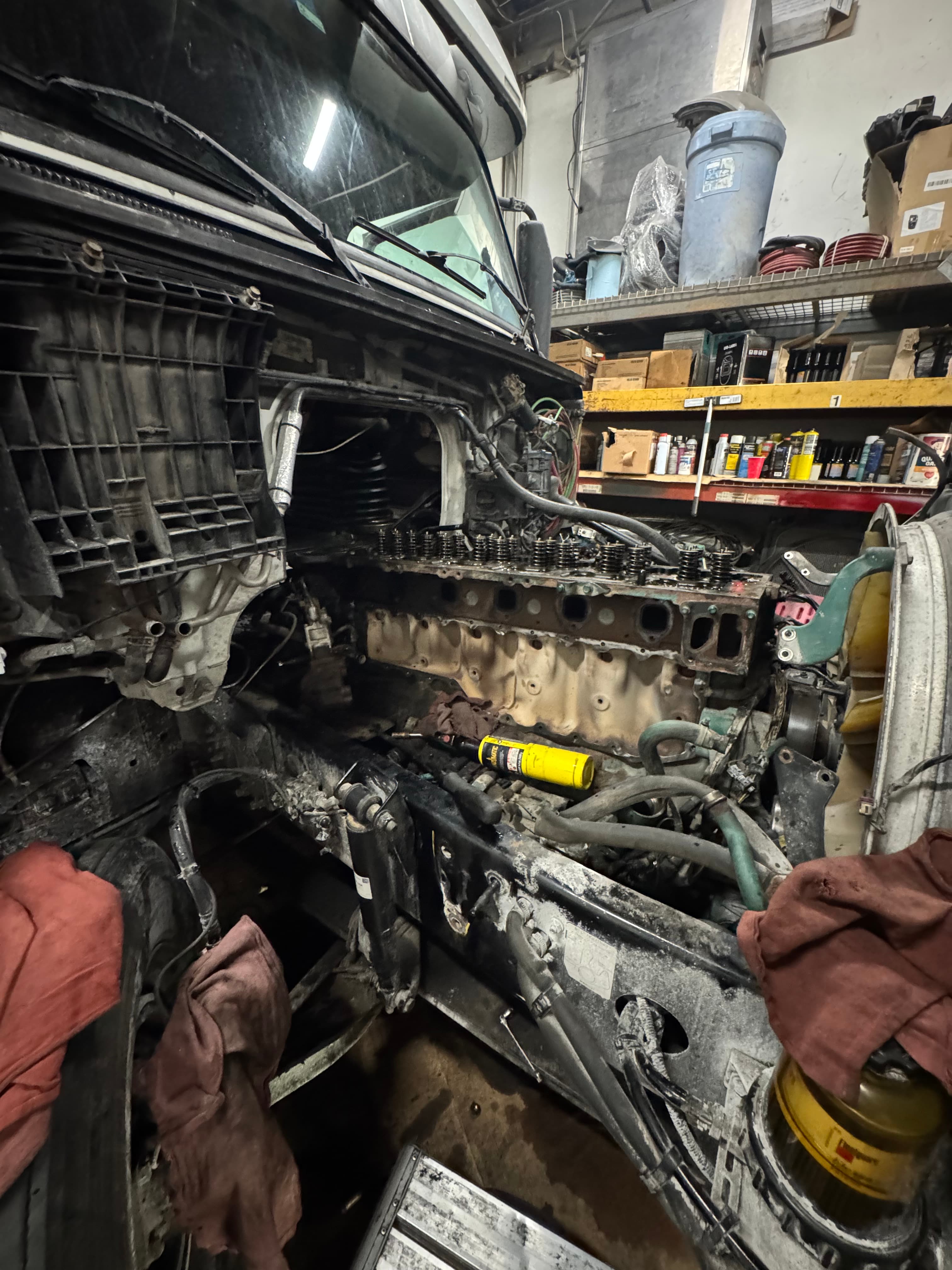 Partially disassembled large truck engine with exposed internal components in a cluttered mechanical workshop.