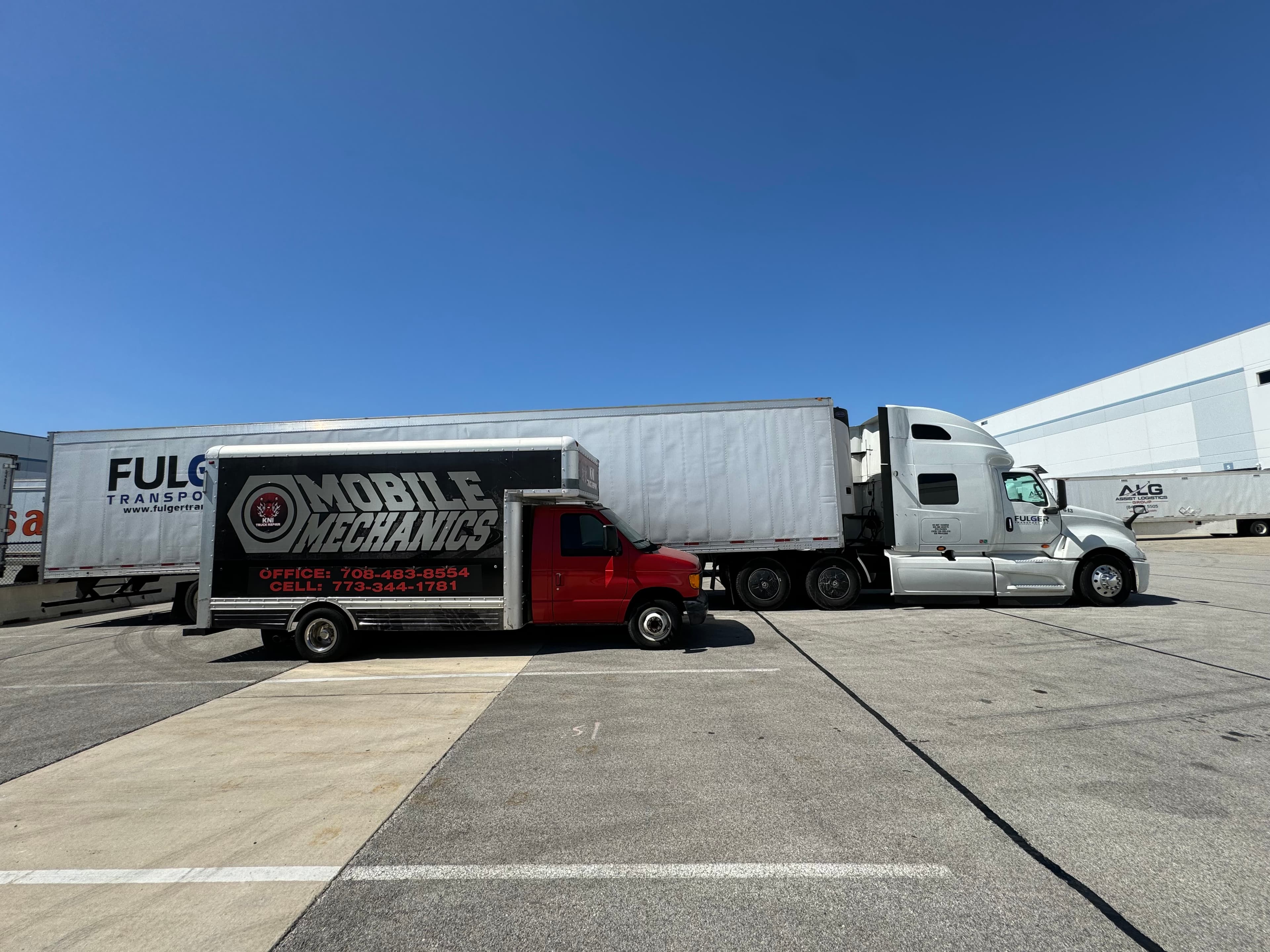 Red mobile mechanics van parked next to a white semi-truck in a sunny parking lot.